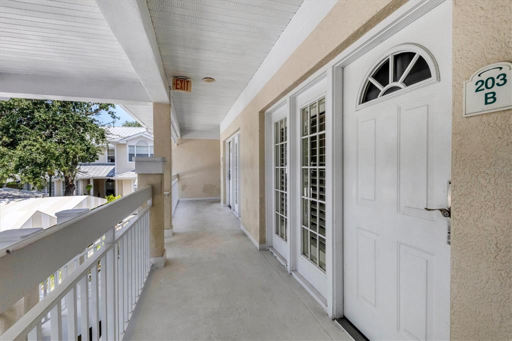 An exterior walkway leads to a white door marked 203 B on a building balcony — 3401 54TH DRIVE W UNIT 203, BRADENTON, FL