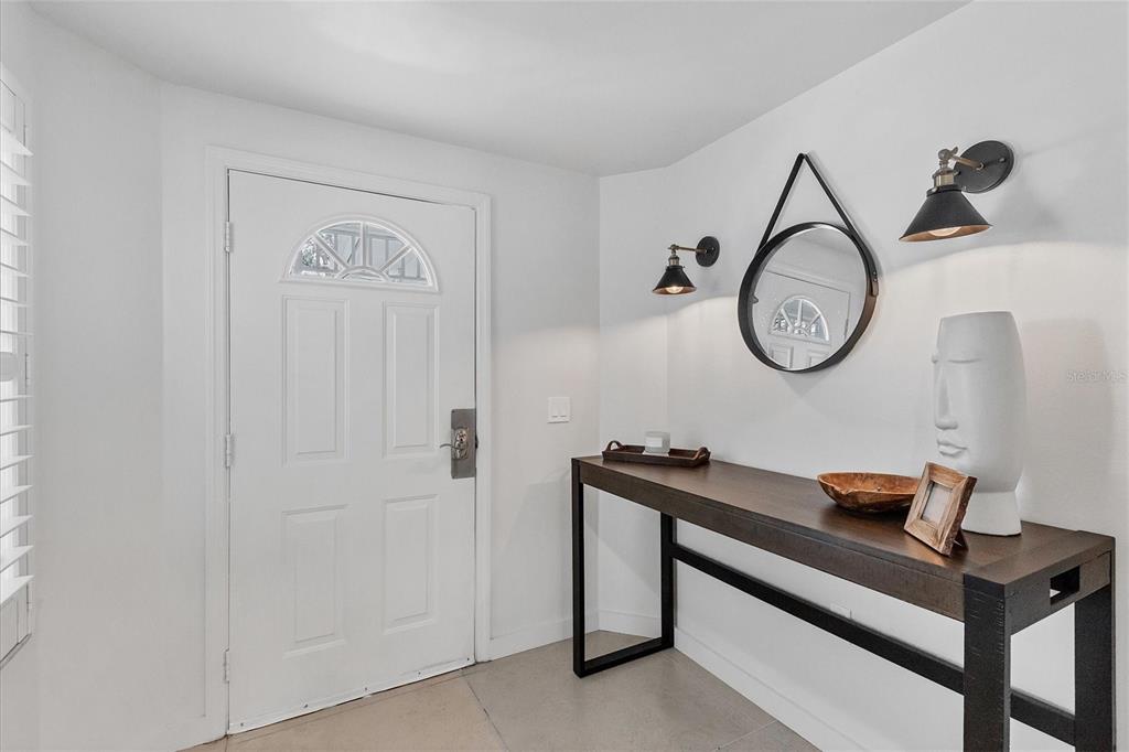 An entryway features a white door, a dark wood console table, and two wall-mounted lamps — 3401 54TH DRIVE W UNIT 203, BRADENTON, FL