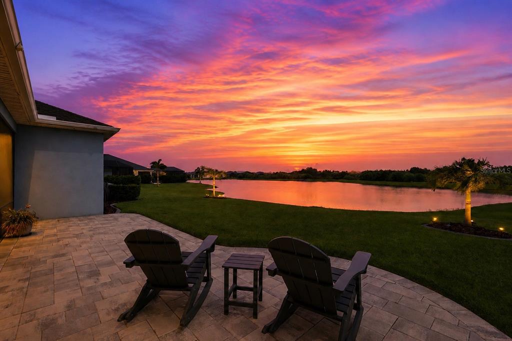 Two dark chairs sit on a stone patio overlooking a lake at sunset — 8611 MERCATOR COURT, PARRISH, FL