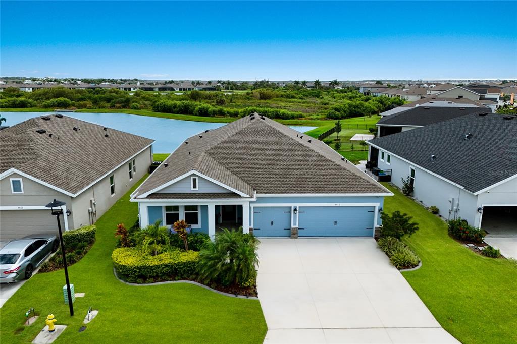 An aerial view shows a blue single-story house with a two-car garage and lakefront backyard — 8611 MERCATOR COURT, PARRISH, FL