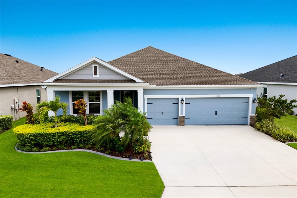A light blue single-story house features a three-car garage and a landscaped front yard — 8611 MERCATOR COURT, PARRISH, FL