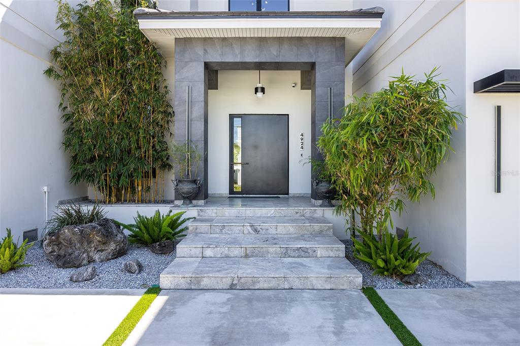 A modern home entrance features a dark door, stone steps, and bamboo landscaping — 4924 W SAN RAFAEL STREET, TAMPA, FL