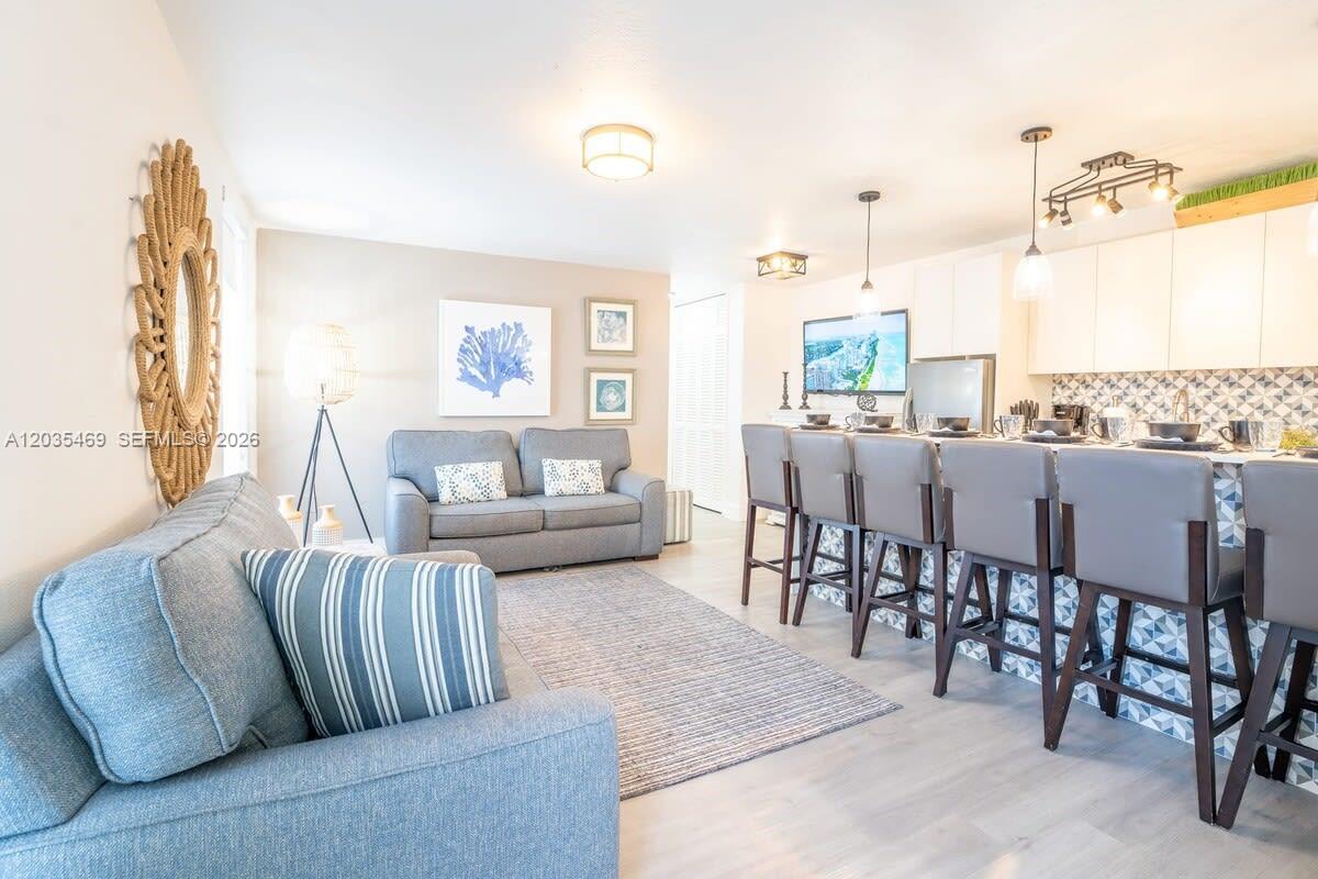A living room features a grey sofa, a patterned rug, and a kitchen island with stools — 7834 abbott ave # 7, Miami Beach FL 33141, MIAMI BEACH, FL