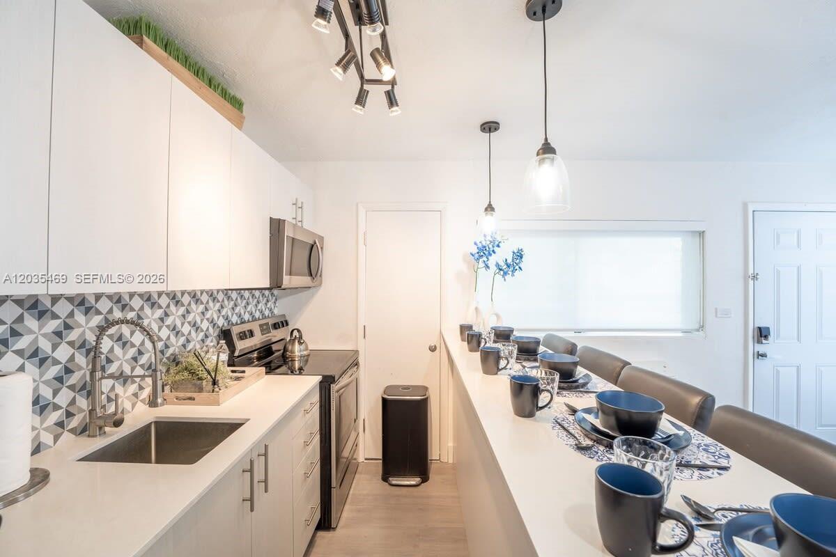 A modern kitchen features white cabinetry, a geometric backsplash, and a breakfast bar with seating — 7834 abbott ave # 7, Miami Beach FL 33141, MIAMI BEACH, FL
