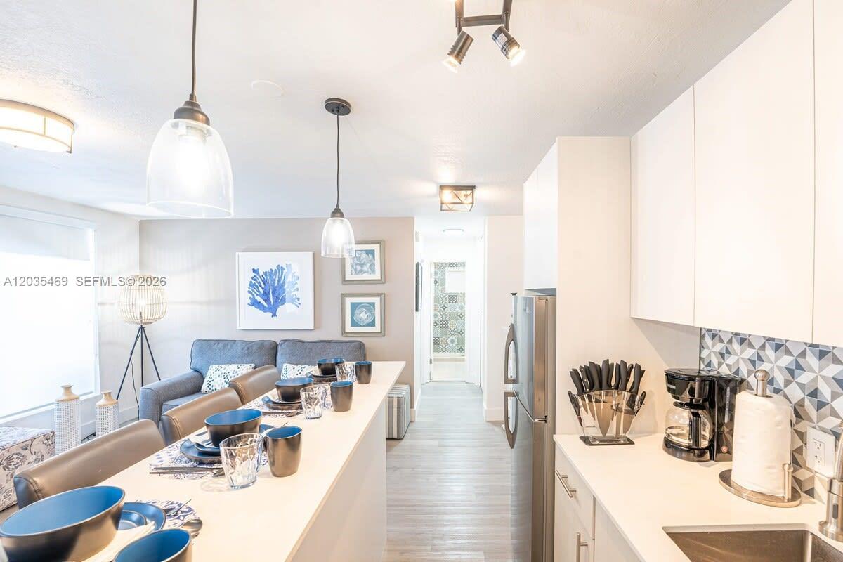 A modern kitchen with white cabinetry and a breakfast bar overlooks a living area — 7834 abbott ave # 7, Miami Beach FL 33141, MIAMI BEACH, FL