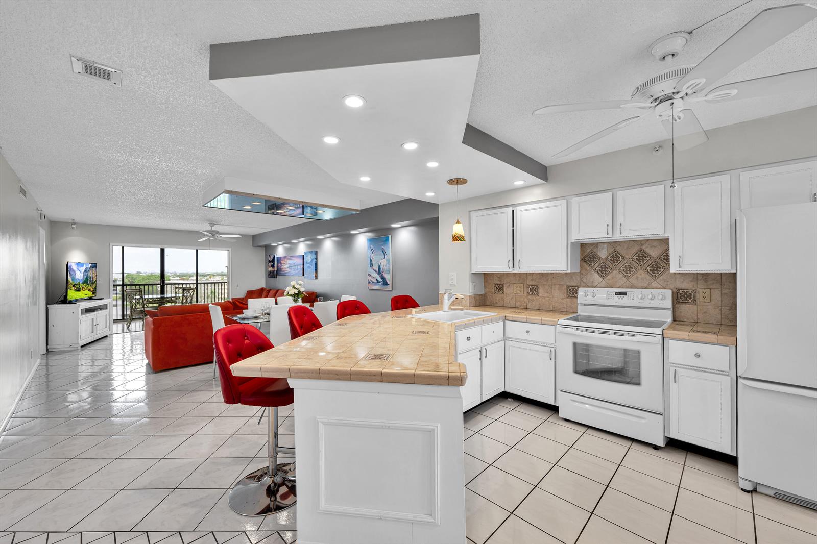 A kitchen with white cabinets and tile countertops opens into a living area with red furniture — 2205 S Cypress Bend Drive # 801, Pompano Beach FL 33069, POMPANO BEACH, FL