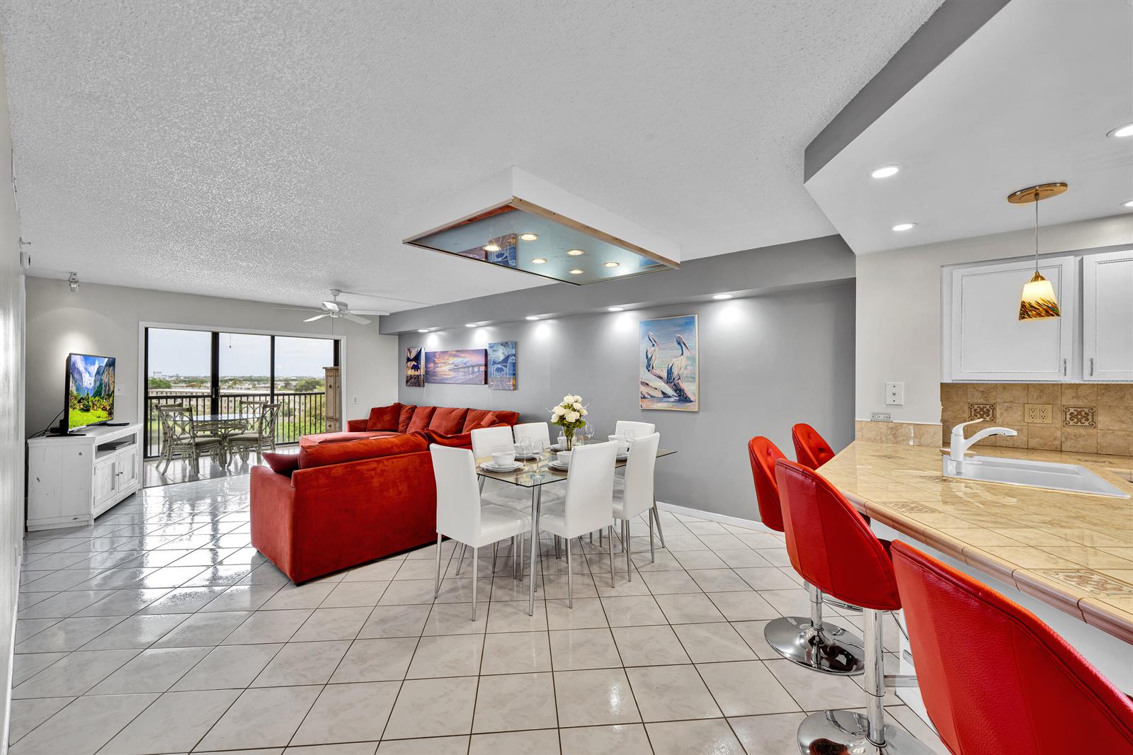An open-concept living and dining area features white tile floors, red furniture, and a kitchen — 2205 S Cypress Bend Drive # 801, Pompano Beach FL 33069, POMPANO BEACH, FL