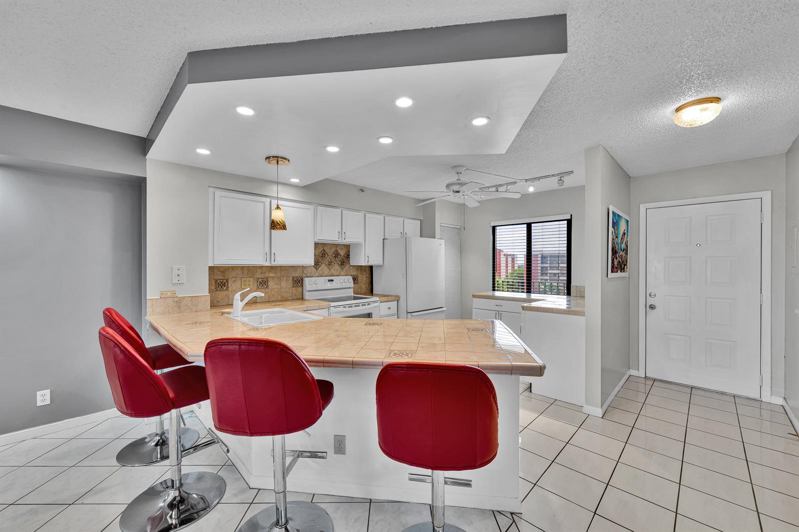 A kitchen with tiled countertops, white cabinets, red bar stools, and a recessed ceiling feature — 2205 S Cypress Bend Drive # 801, Pompano Beach FL 33069, POMPANO BEACH, FL