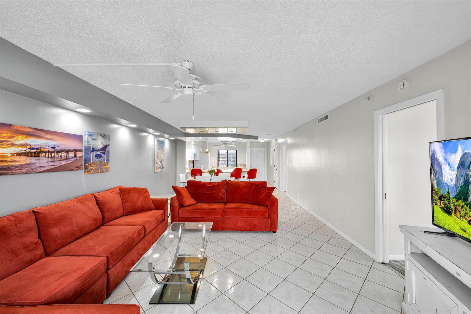 A living room features two red sofas, a glass coffee table, and tile flooring — 2205 S Cypress Bend Drive # 801, Pompano Beach FL 33069, POMPANO BEACH, FL