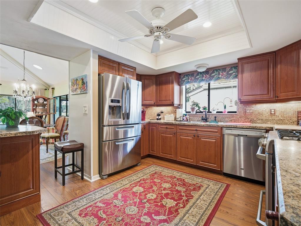 A kitchen features wood cabinets, stainless steel appliances, granite countertops, and a red area rug — 718 TANTALLON COURT, NEW SMYRNA BEACH, FL