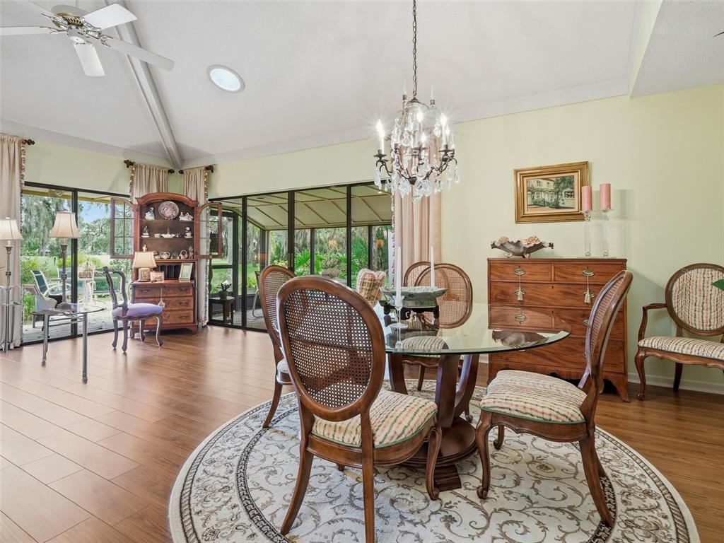 A dining room features a glass table, chandelier, wooden furniture, and large sliding glass doors — 718 TANTALLON COURT, NEW SMYRNA BEACH, FL