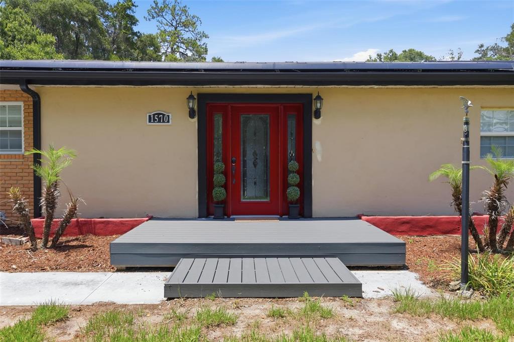 A front exterior view of a house featuring a red door and a gray deck — 1570 GLENWOOD ROAD, DELAND, FL