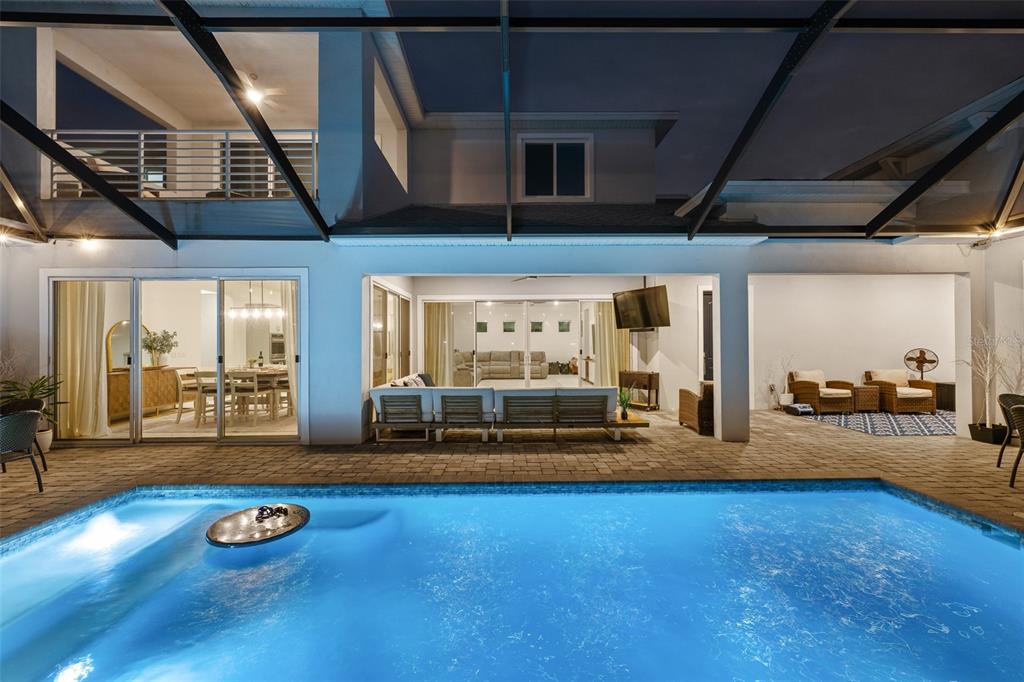 A backyard swimming pool sits in front of a covered patio with outdoor seating — 8776 IVY STARK BOULEVARD, WESLEY CHAPEL, FL
