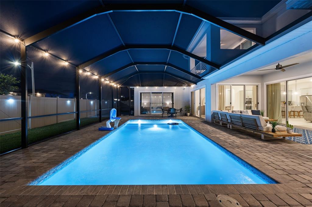 A rectangular swimming pool sits on a paved patio inside a screened-in outdoor enclosure — 8776 IVY STARK BOULEVARD, WESLEY CHAPEL, FL