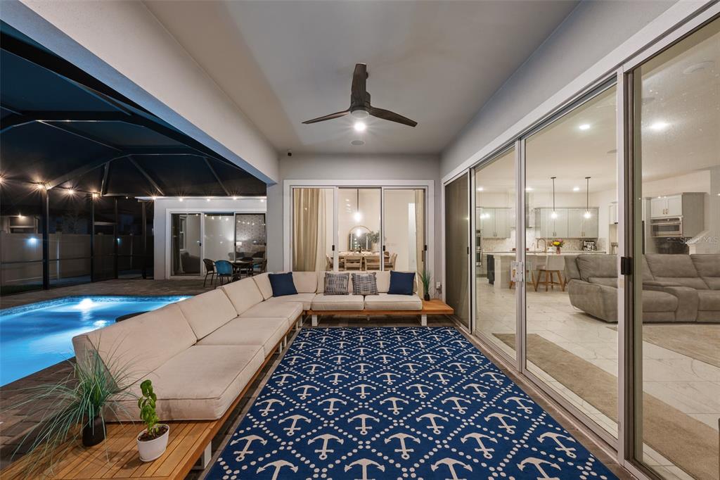 A covered patio features a sectional sofa, an anchor-patterned rug, and a view of a pool — 8776 IVY STARK BOULEVARD, WESLEY CHAPEL, FL
