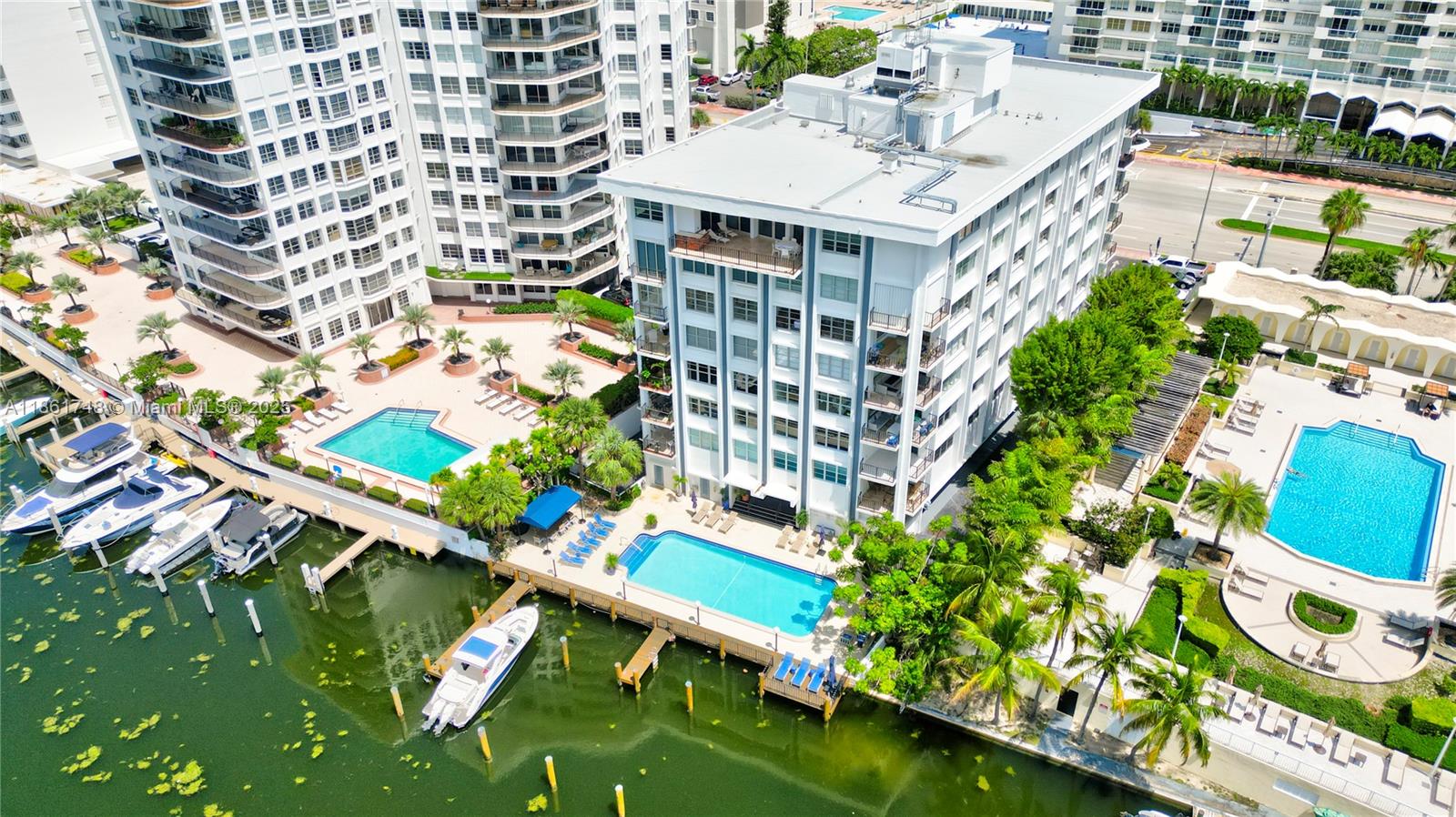 An aerial view shows a waterfront apartment building with two swimming pools and docked boats — 5640 Collins Ave # 6B, Miami Beach FL 33140, MIAMI BEACH, FL