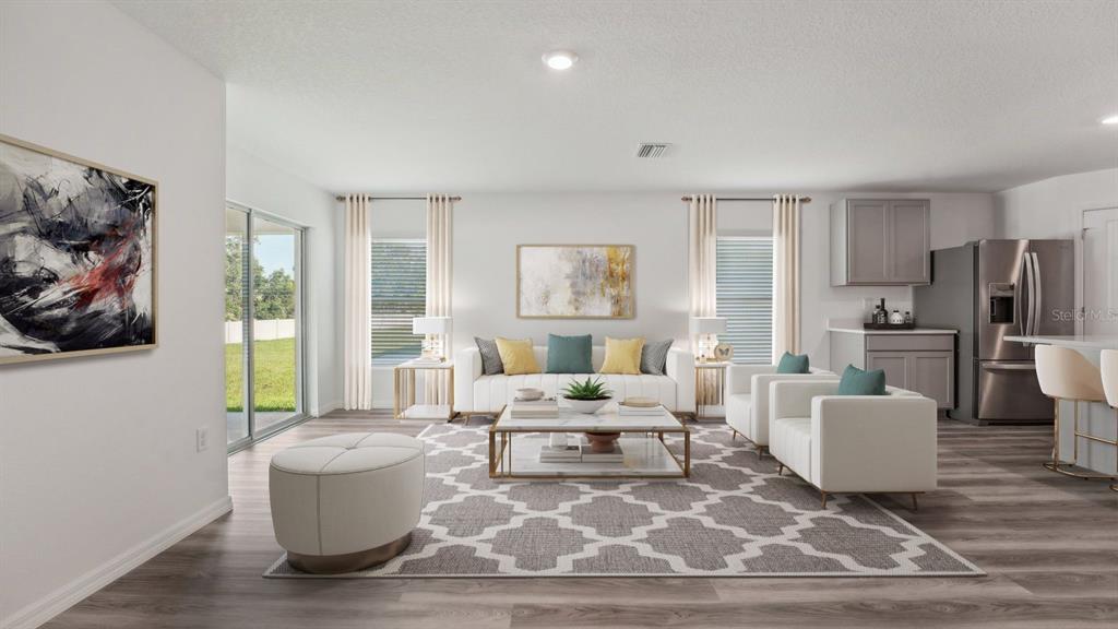 A bright living room features a white sofa, patterned rug, and open kitchen area — 18700 HIGHLAND DEW STREET, SPRING HILL, FL