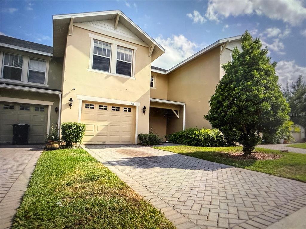 A two-story townhouse with a beige stucco exterior, a single-car garage, and a paved driveway — 9734 TIRAMASU TRAIL, ORLANDO, FL