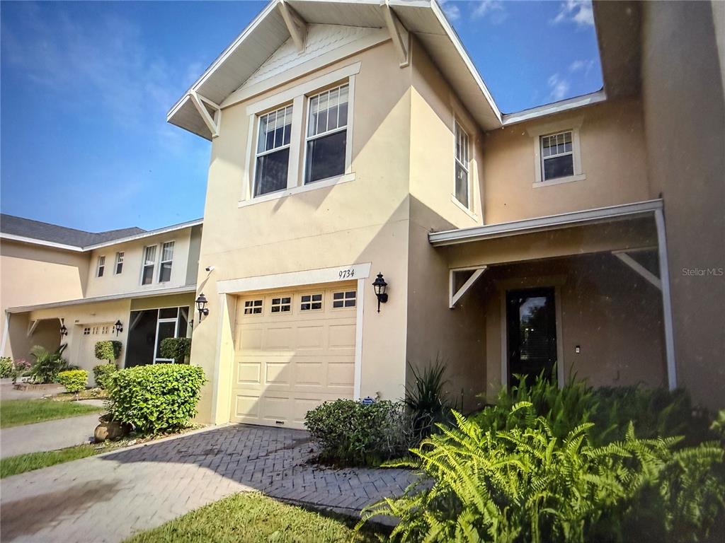 A two-story tan stucco townhouse features a single-car garage and a covered front entryway — 9734 TIRAMASU TRAIL, ORLANDO, FL