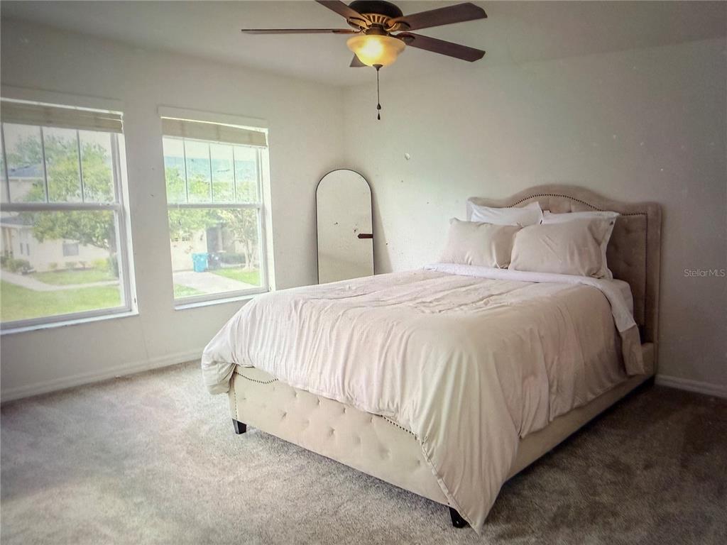 A bedroom features a tufted beige bed, a floor mirror, and a ceiling fan — 9734 TIRAMASU TRAIL, ORLANDO, FL
