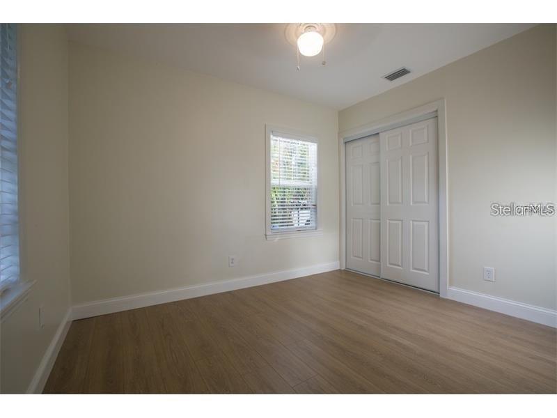 An empty bedroom features light-colored walls, wood-look flooring, a window, and a sliding closet door — 908 W OHIO AVENUE, TAMPA, FL