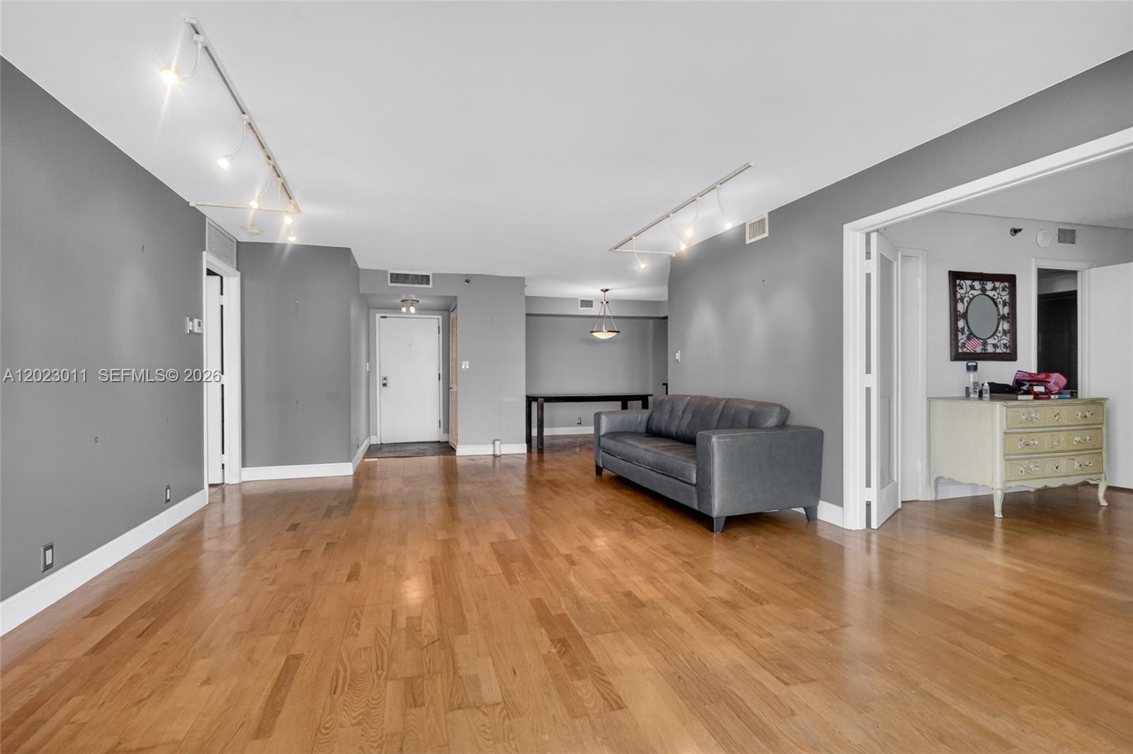 A living room features gray walls, hardwood floors, track lighting, and a dark gray sofa — 2000 Towerside Ter # 709, Miami FL 33138, MIAMI, FL