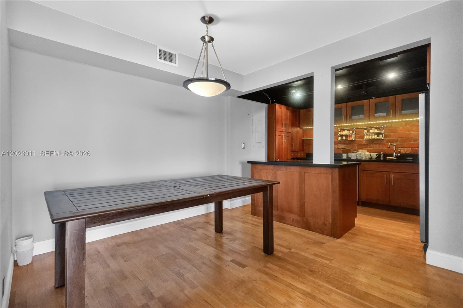 A dining area with a wooden table sits adjacent to an open kitchen with brick walls — 2000 Towerside Ter # 709, Miami FL 33138, MIAMI, FL