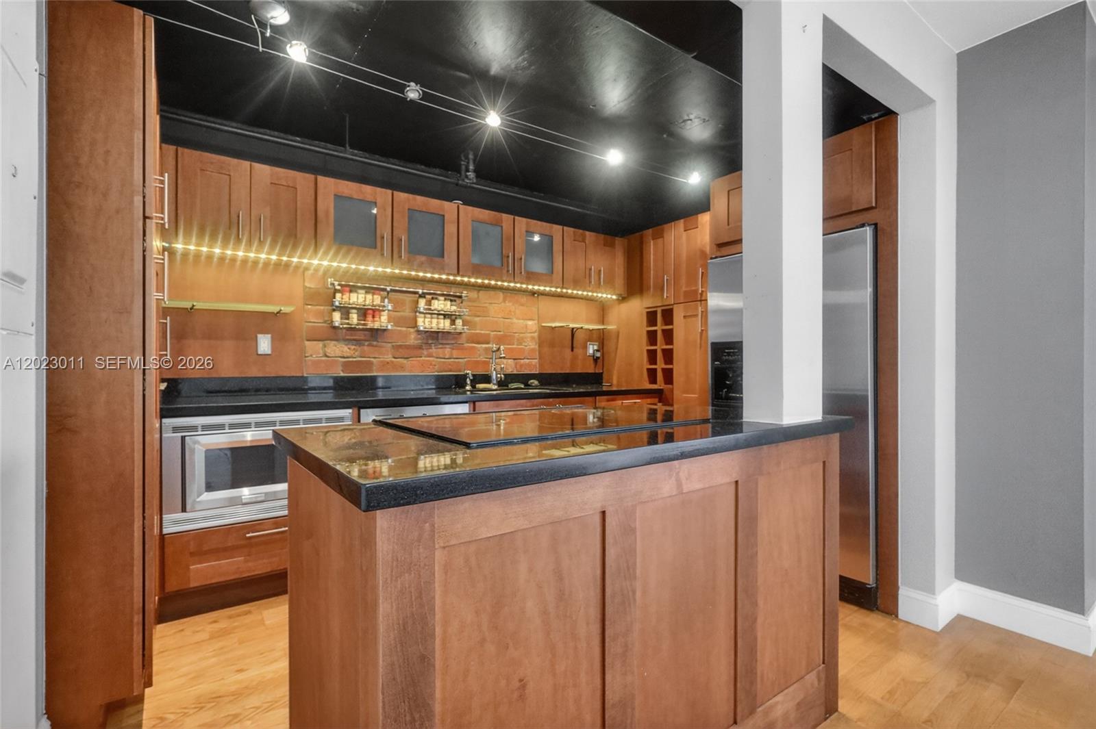 A kitchen features wood cabinets, a brick backsplash, black countertops, and a black ceiling — 2000 Towerside Ter # 709, Miami FL 33138, MIAMI, FL