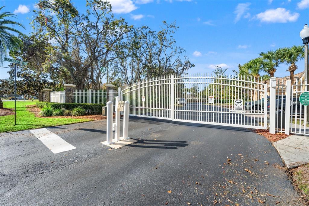 A white metal gate secures the entrance to a residential community with mature trees — 7305 GABERIA ROAD, NEW PORT RICHEY, FL