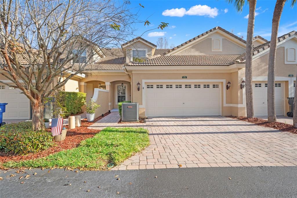 A beige townhome with a two-car garage, a paver driveway, and a small front yard — 7305 GABERIA ROAD, NEW PORT RICHEY, FL