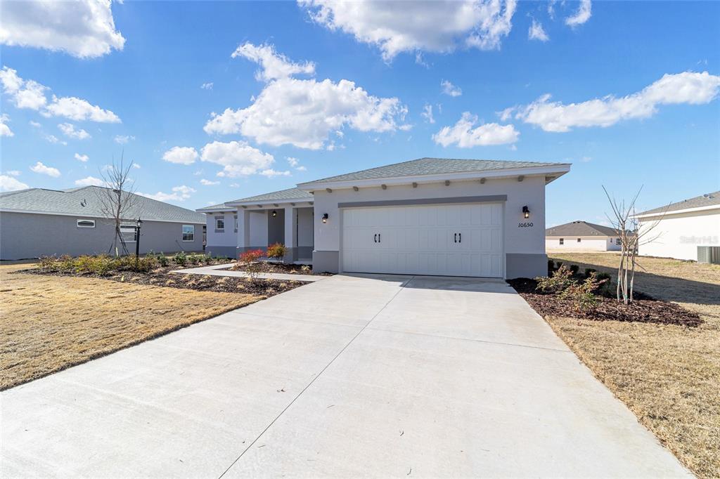 A single-story house with a two-car garage and a concrete driveway under a blue sky — 10650 SW 101ST LANE ROAD, OCALA, FL