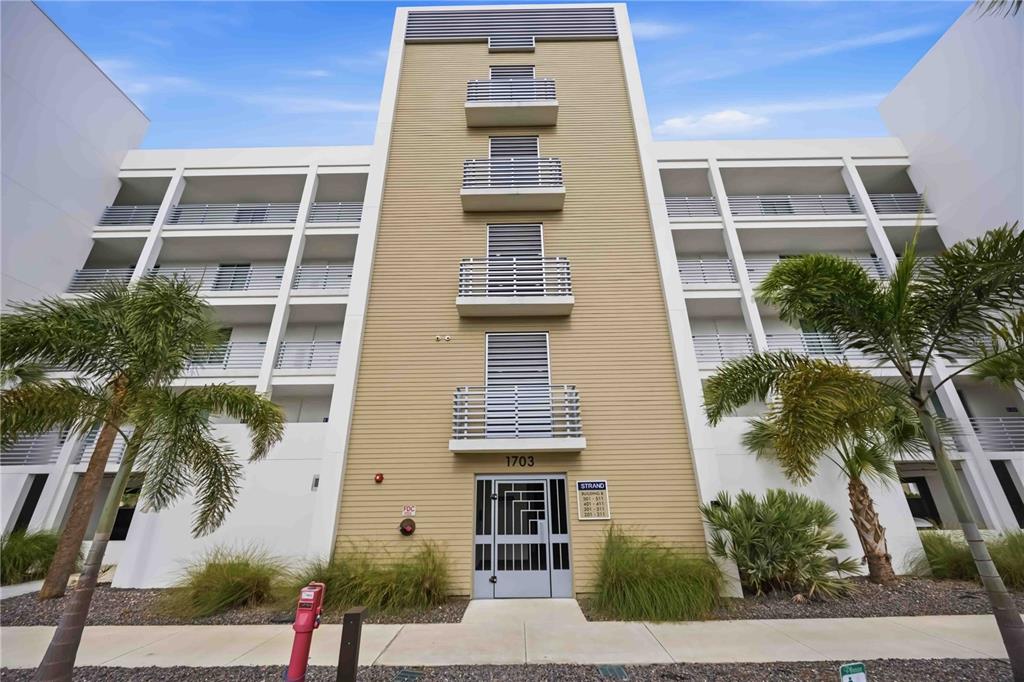 A multi-story apartment building exterior features a tan central section with balconies and white wings — 1703 N TAMIAMI TRAIL UNIT 406, SARASOTA, FL