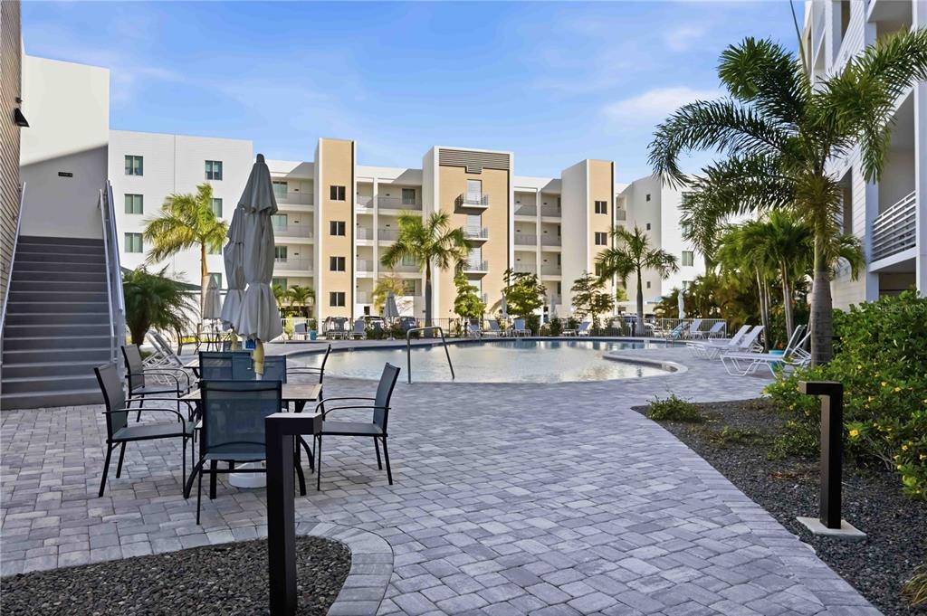 A paved patio with outdoor seating overlooks a swimming pool surrounded by multi-story apartment buildings — 1703 N TAMIAMI TRAIL UNIT 406, SARASOTA, FL