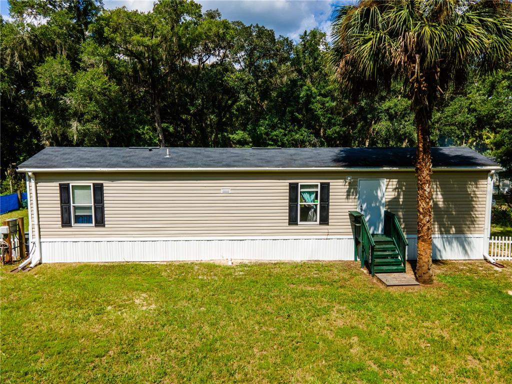 A single-story mobile home with tan siding, black shutters, and a green wooden staircase — 14388 NE 116TH TERRACE, FORT MC COY, FL