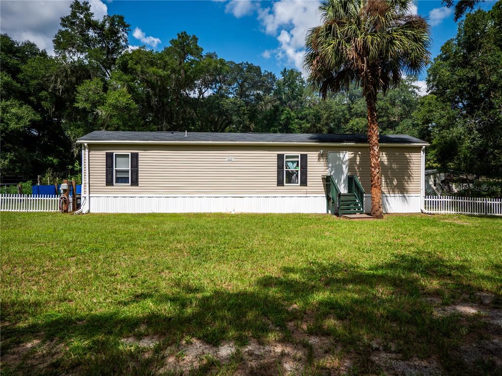 A single-story manufactured home with tan siding and a white picket fence in a yard — 14388 NE 116TH TERRACE, FORT MC COY, FL