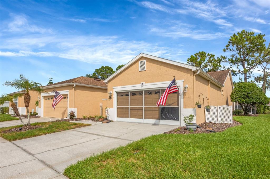 Two adjacent tan stucco houses with garages and American flags under a blue sky — 20828 EUSTIS ROAD, LAND O LAKES, FL