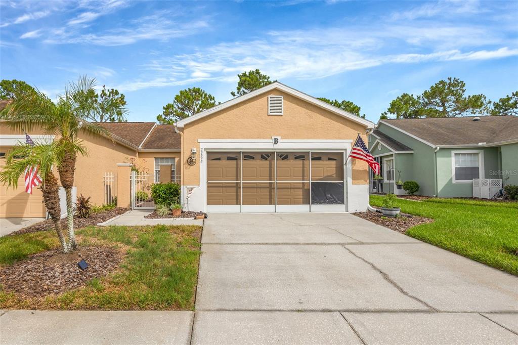 A single-story house with a tan stucco exterior, a two-car garage, and an American flag — 20828 EUSTIS ROAD, LAND O LAKES, FL