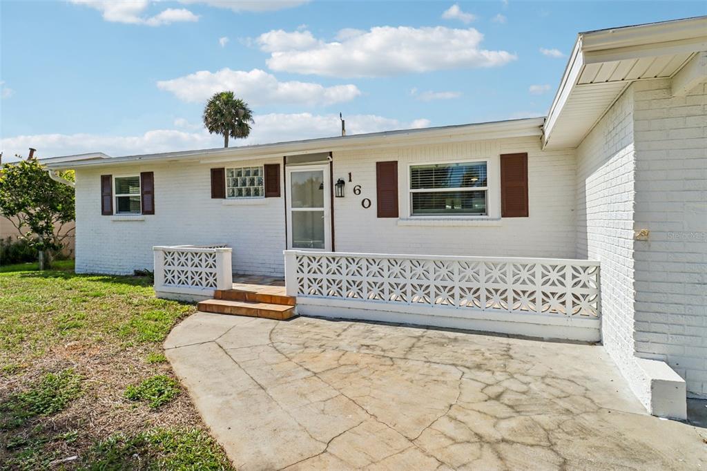 A white brick house exterior features a concrete patio, decorative block railing, and brown shutters — 160 PONCE DE LEON DRIVE, ORMOND BEACH, FL