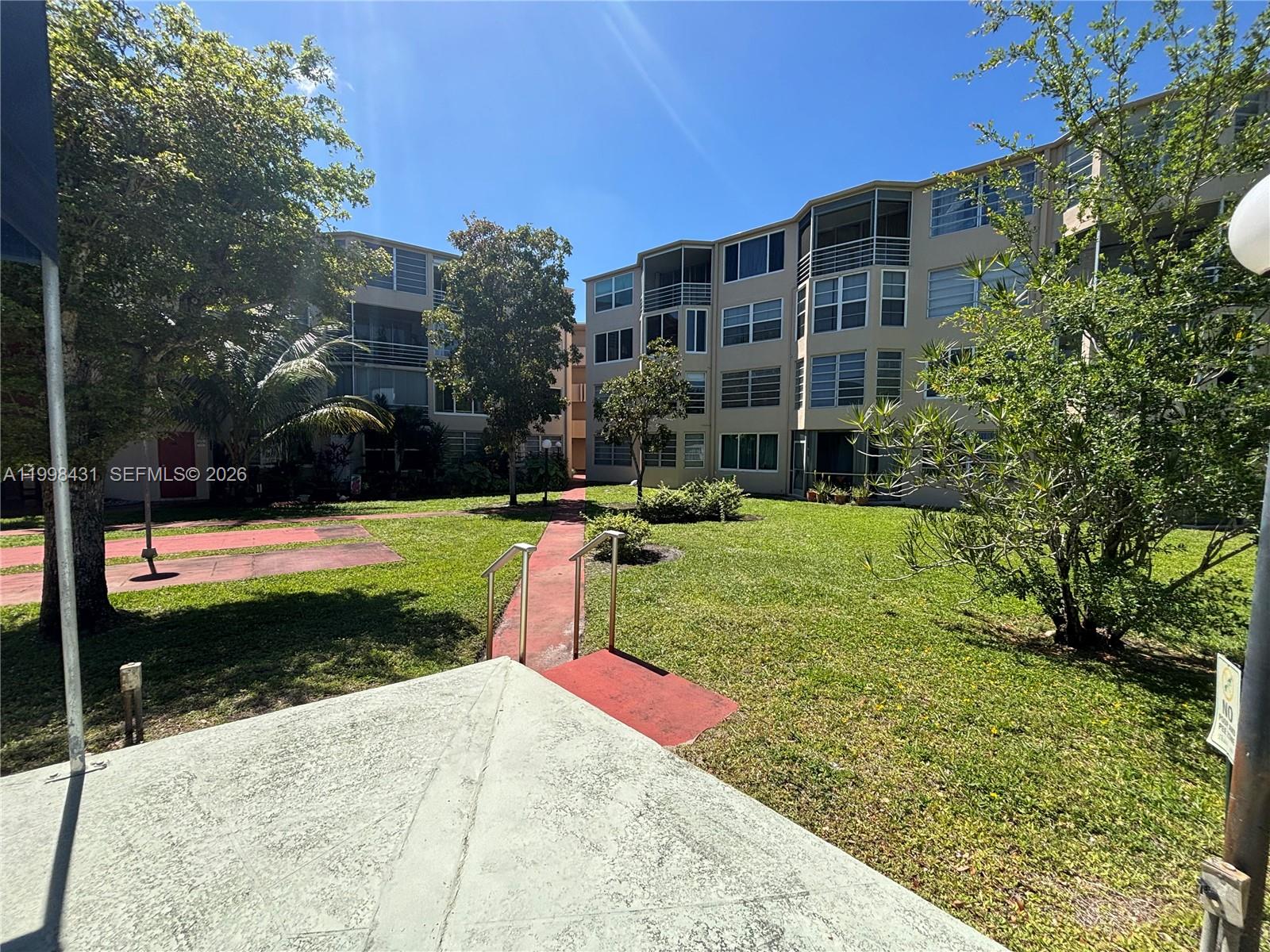 A multi-story apartment building overlooks a grassy courtyard with a red pedestrian walkway — 1501 NE 191st St # C211, Miami FL 33179, MIAMI, FL