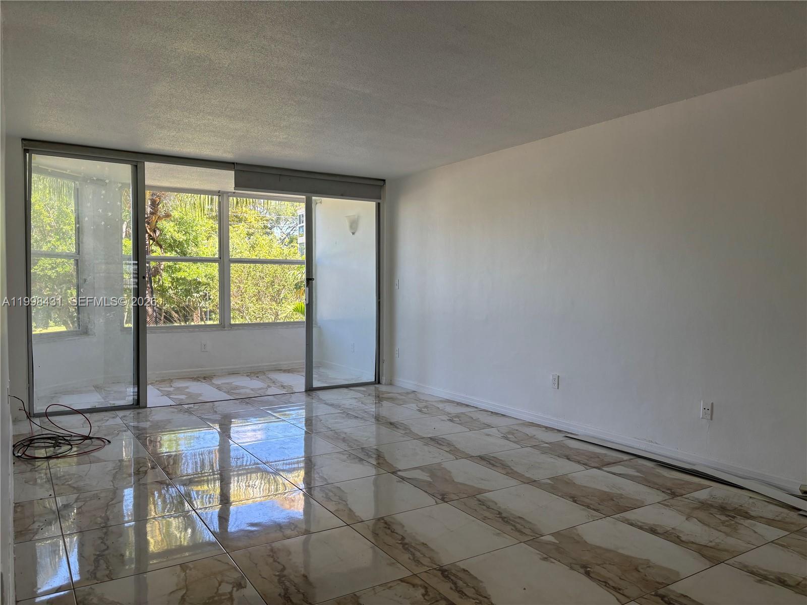 An empty room features white walls, large marble-patterned floor tiles, and a sliding glass door — 1501 NE 191st St # C211, Miami FL 33179, MIAMI, FL