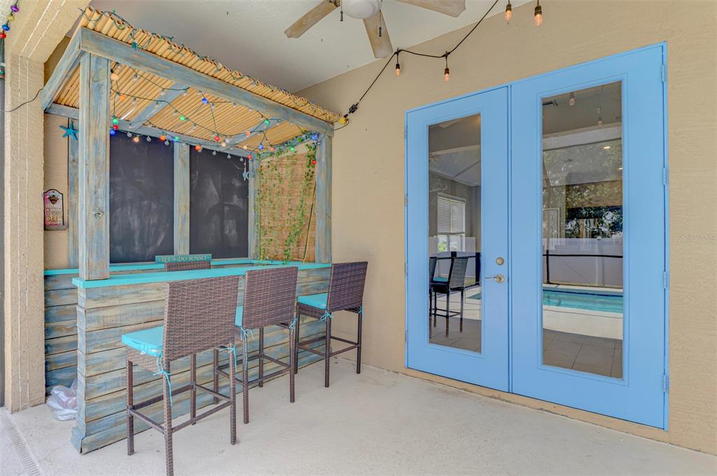 A covered patio features a tiki-style bar with three wicker stools and blue double doors — 4327 MANFIELD DRIVE, VENICE, FL