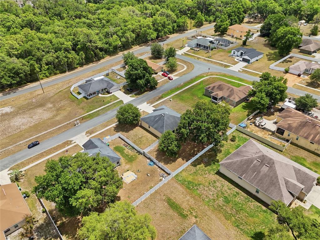 An aerial view shows several suburban houses with fenced yards and trees along paved streets — 306 STONEPOINT LANE, LADY LAKE, FL