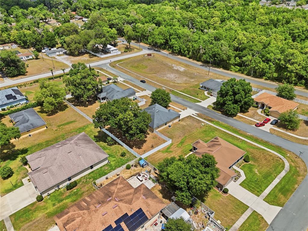 An aerial view shows several suburban houses with yards and driveways near a wooded area — 306 STONEPOINT LANE, LADY LAKE, FL