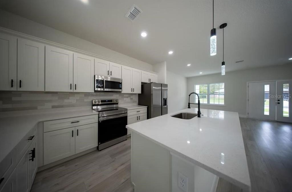 A modern kitchen features white cabinets, stainless steel appliances, and a large quartz-topped island — 3286 W CRANDON DRIVE, CITRUS SPRINGS, FL