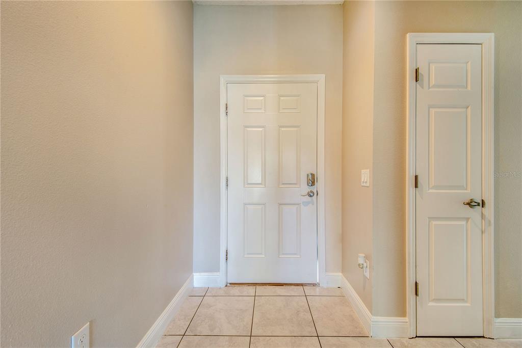 An entryway features light-colored tile flooring, beige walls, a white front door, and a closet — 1608 PILCHARD COURT, POINCIANA, FL