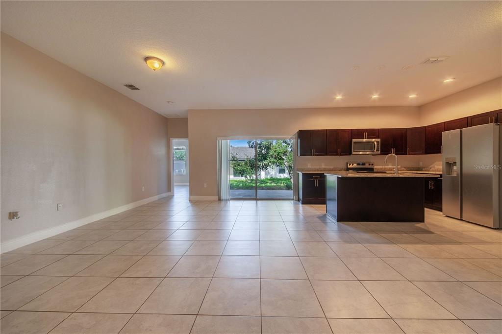 An open-concept kitchen and living area features tile flooring, dark wood cabinets, and sliding glass doors — 1608 PILCHARD COURT, POINCIANA, FL