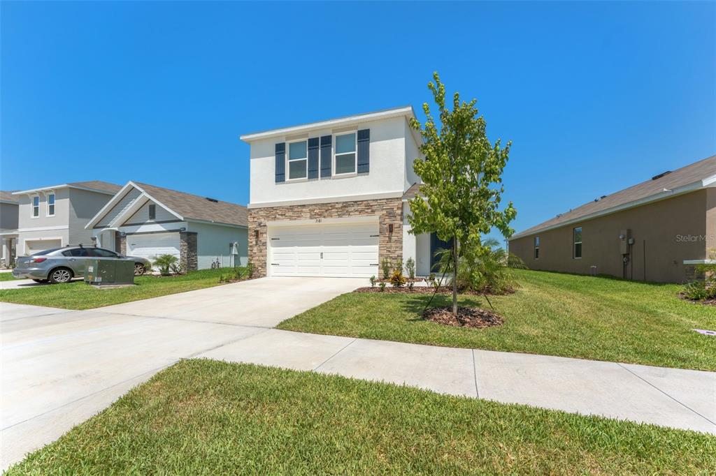 A two-story house with a stone-accented facade, white garage door, and a front lawn — 7181 BROAD RIVER AVENUE, LAND O LAKES, FL