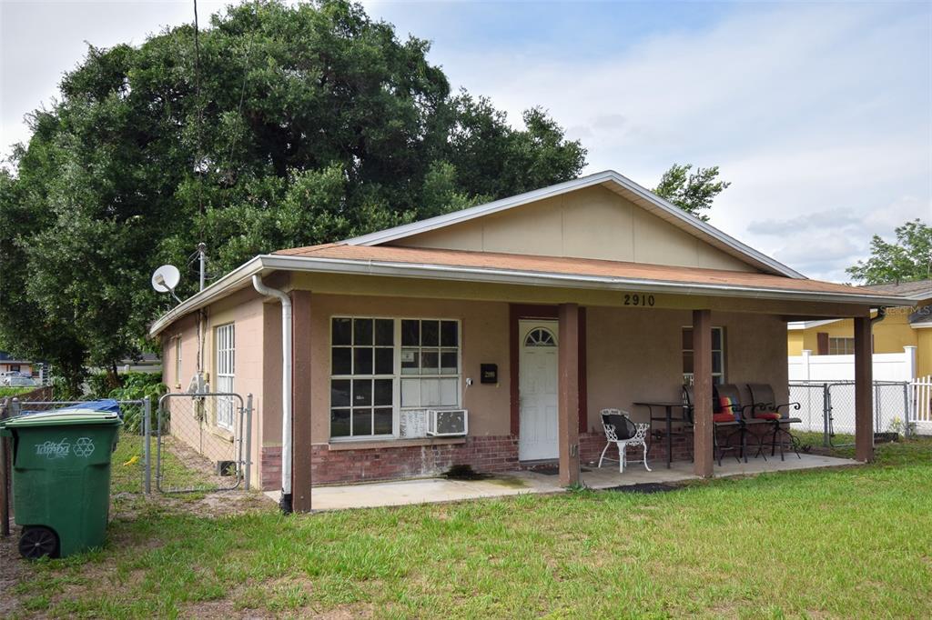 A single-story house with a covered front porch, tan stucco walls, and a brick base — 2910 E 25TH AVENUE, TAMPA, FL