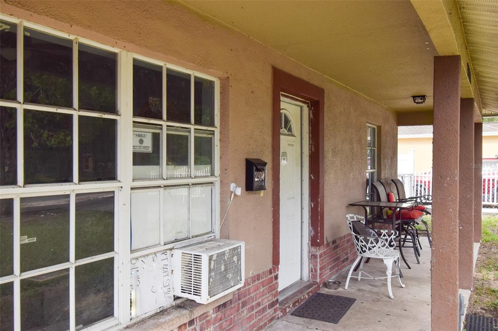 A covered porch features a white front door, a window air conditioner, and patio furniture — 2910 E 25TH AVENUE, TAMPA, FL