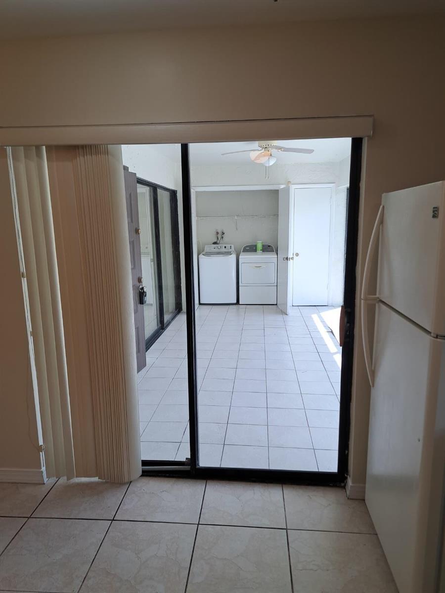 A view through a sliding glass door into a tiled laundry room with appliances — 9330 SW 61st Way # D, Boca Raton FL 33428, BOCA RATON, FL